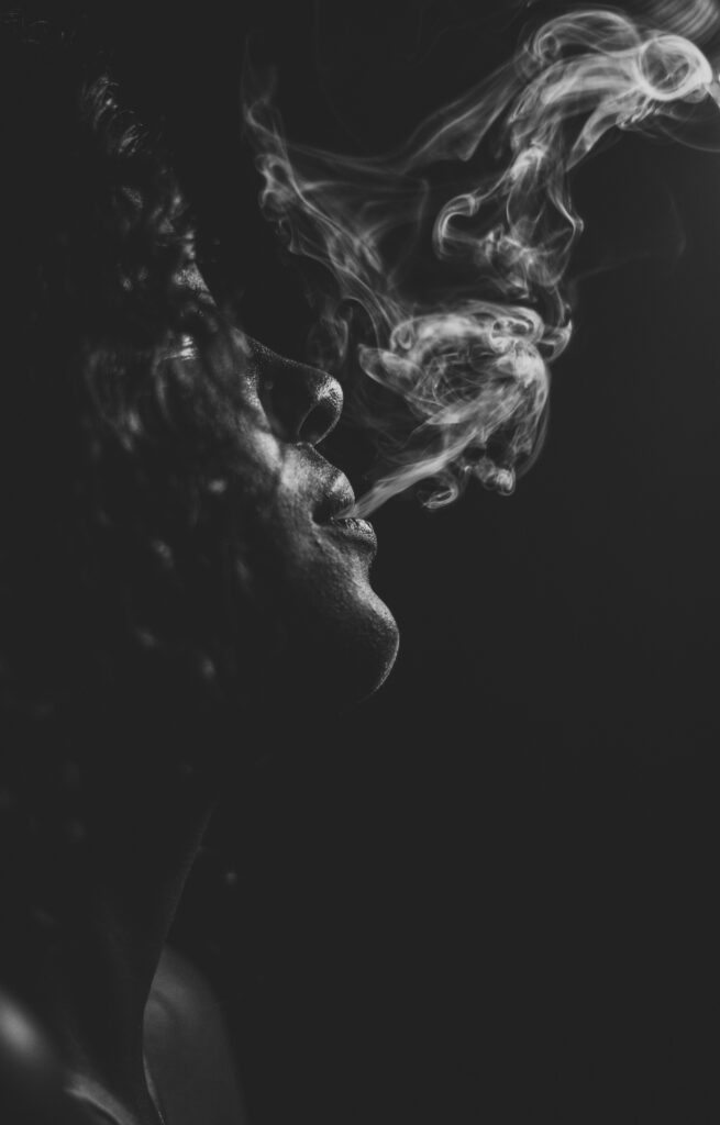 Black and white photo of a woman blowing smoke out of her mouth. 